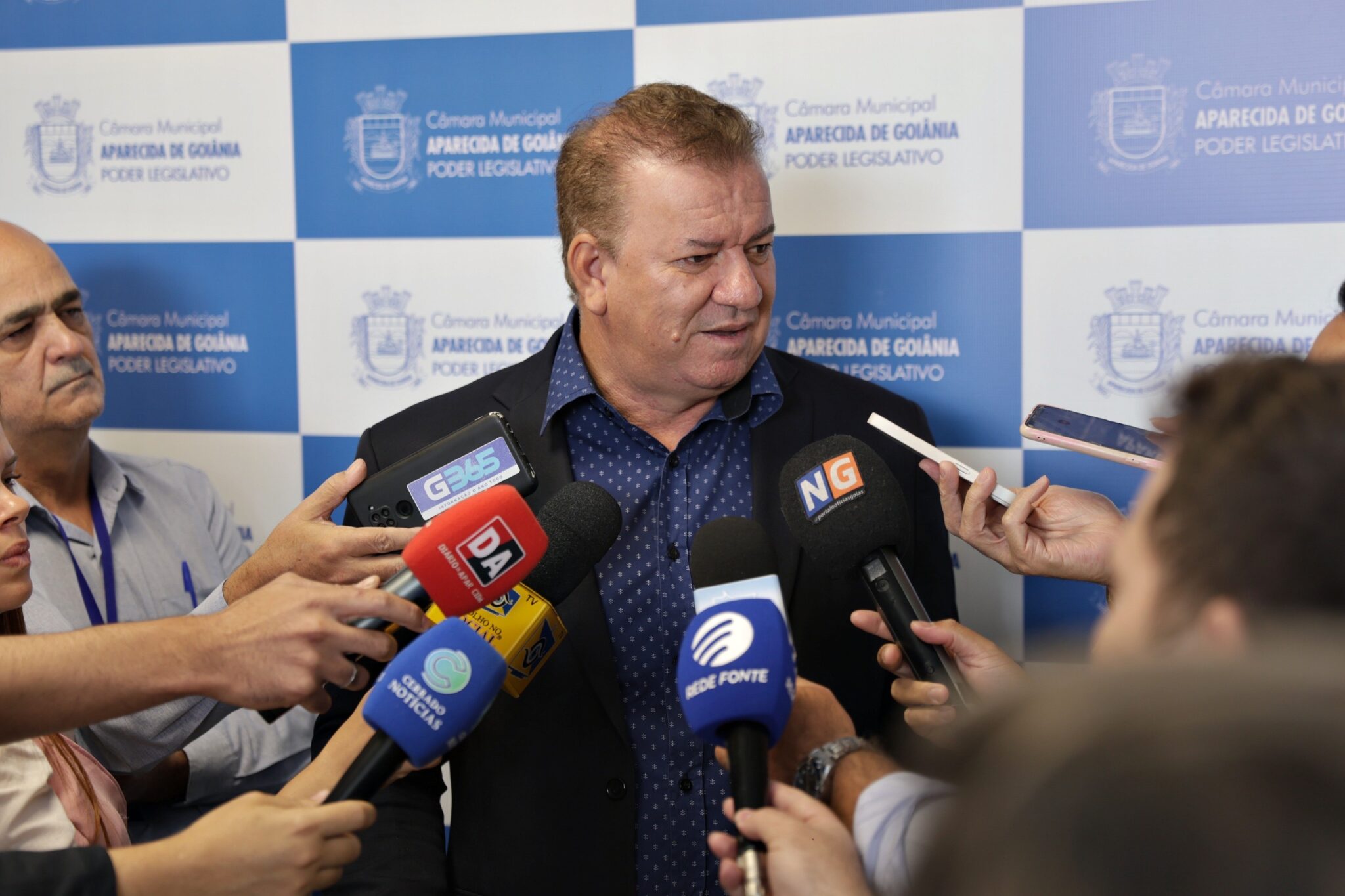 Homem dá entrevista cercado por microfones.