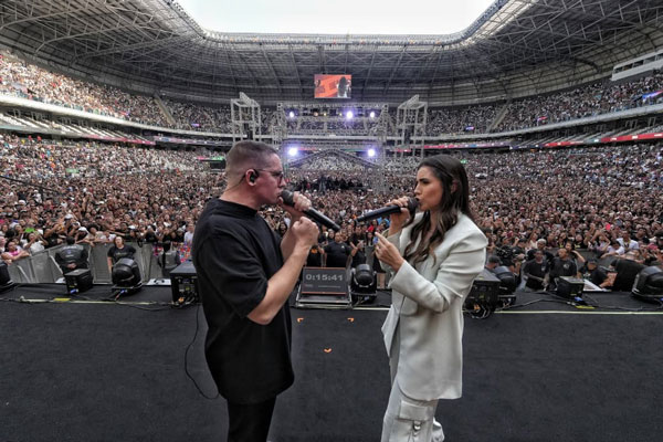 Duas pessoas cantando em estádio lotado.